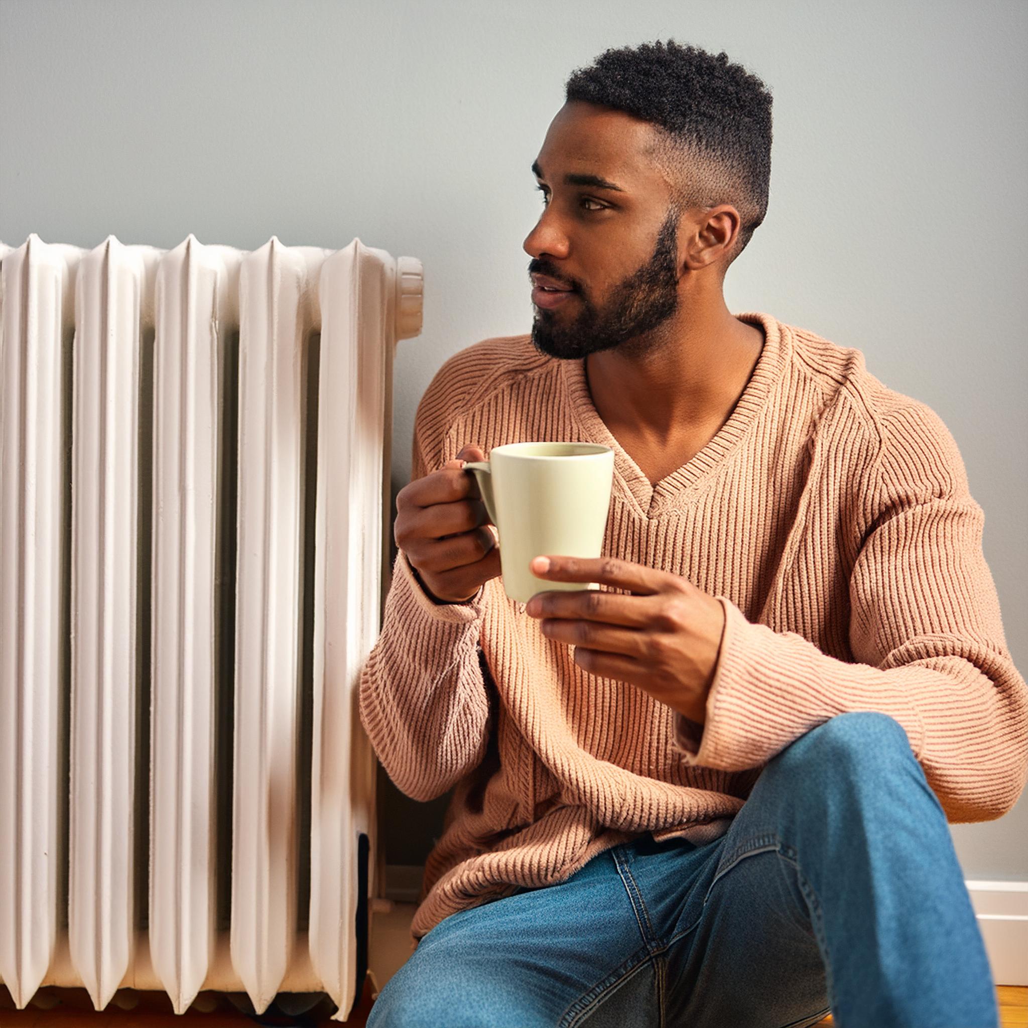 Persona tomando café cerca de un radiador pensando en la tarifa gas tur